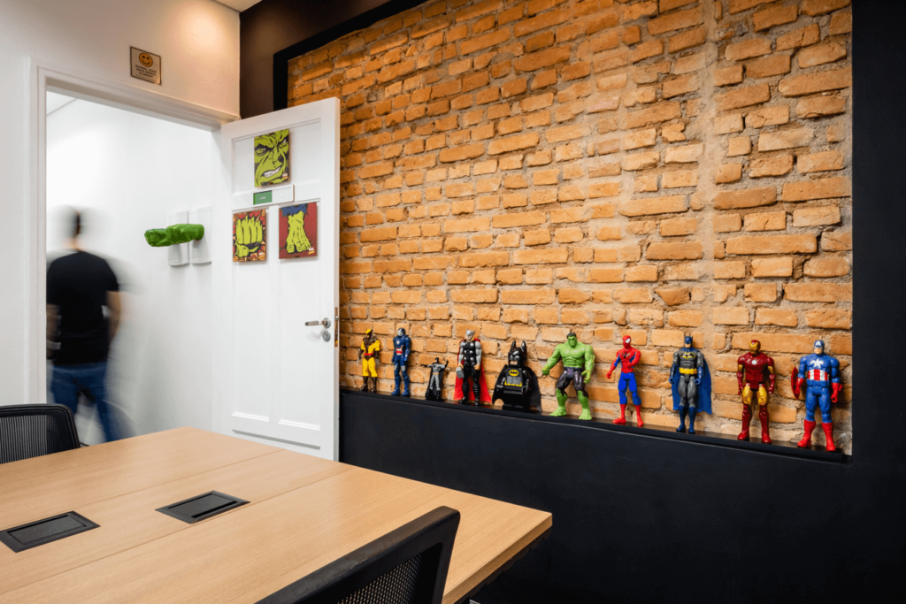 Imagem mostra sala de reunião da Blocktime Coworking com decoração de super-heróis e parede de tijolos