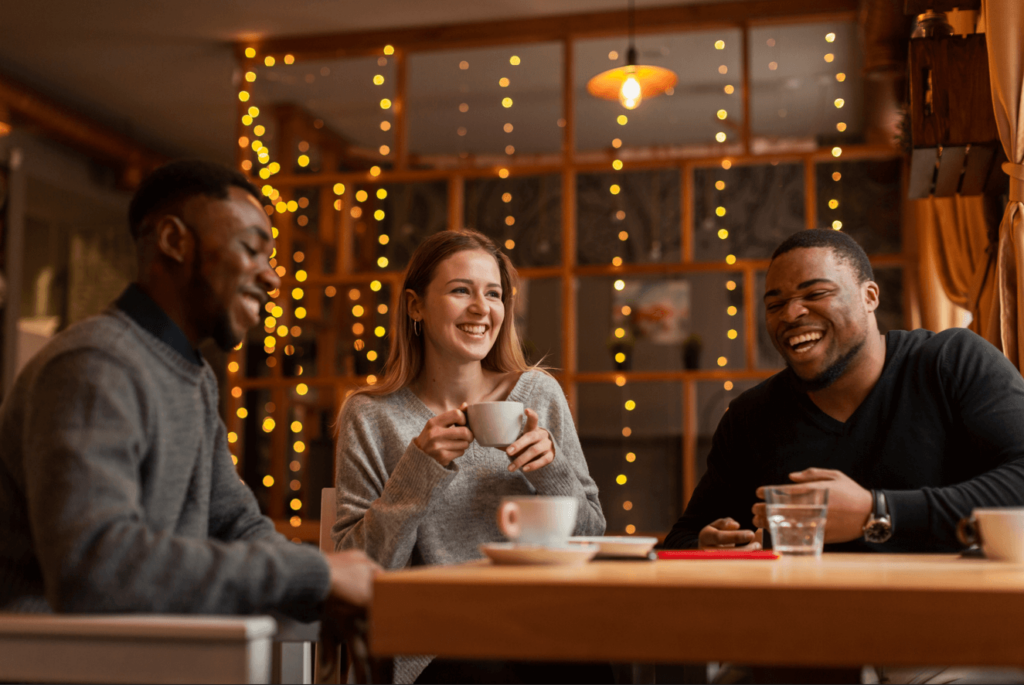 Imagem mostra 3 pessoas tomando café em um restaurante, enquanto dão risada