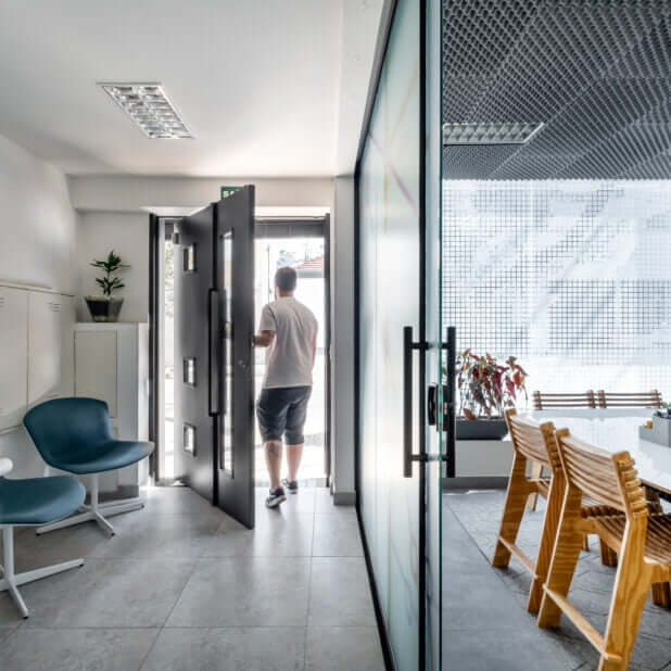 Imagem mostra homem de costas, saindo do espaço da Blocktime Coworking. Ele está abrindo a porta em direção a rua.