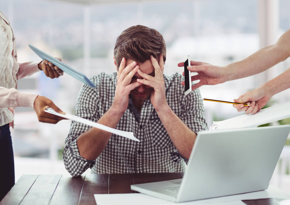 Profissional com as mãos no rosto diante de demandas simultâneas, representando pressão e sobrecarga no ambiente de trabalho.
