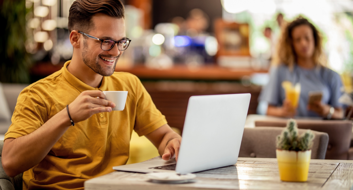 Imagem mostra pessoa trabalhando em um espaço de coworking, tomando um café enquanto faz reunião no computador