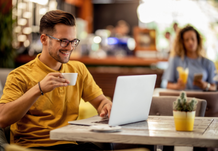 Imagem mostra pessoa trabalhando em um espaço de coworking, tomando um café enquanto faz reunião no computador