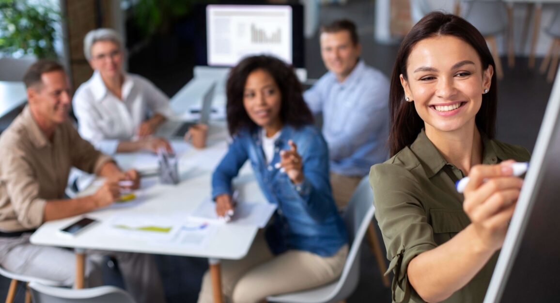 Imagem mostra pessoas diversas em uma sala de coworking, trabalhando e sorrindo em direção a camera