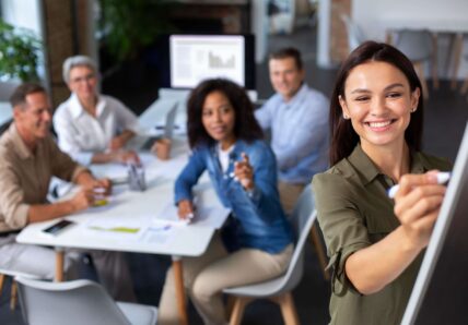 Imagem mostra pessoas diversas em uma sala de coworking, trabalhando e sorrindo em direção a camera