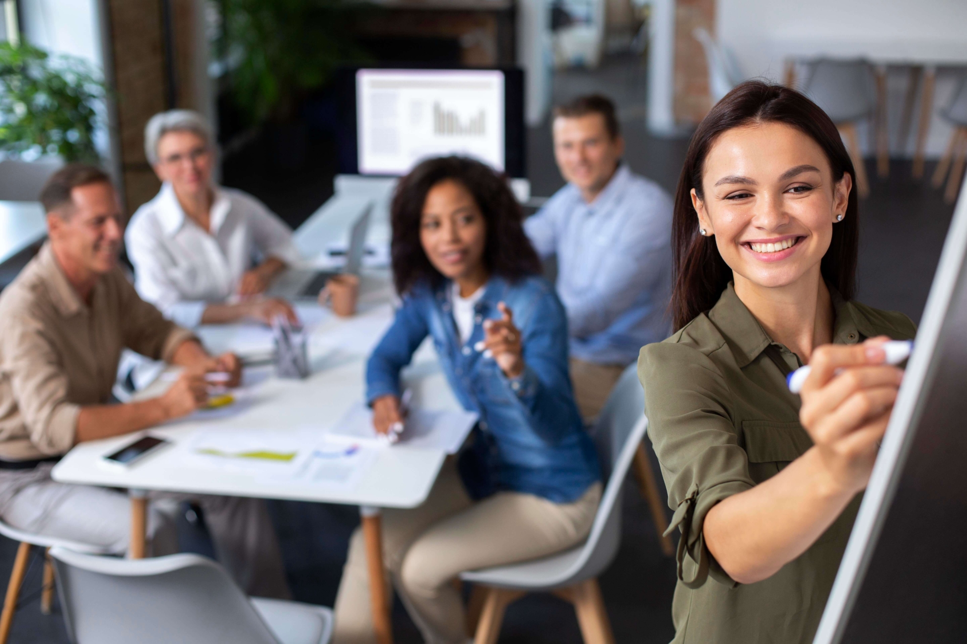 Imagem mostra pessoas diversas em uma sala de coworking, trabalhando e sorrindo em direção a camera
