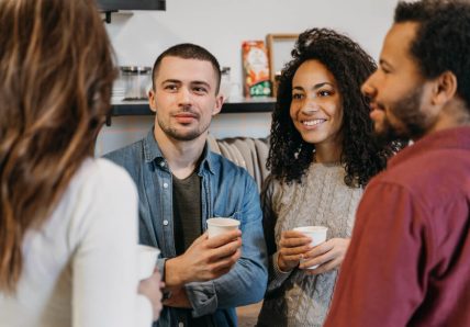Imagem mostra um grupo de 4 pessoas concentradas, conversando, enquanto tomam um café