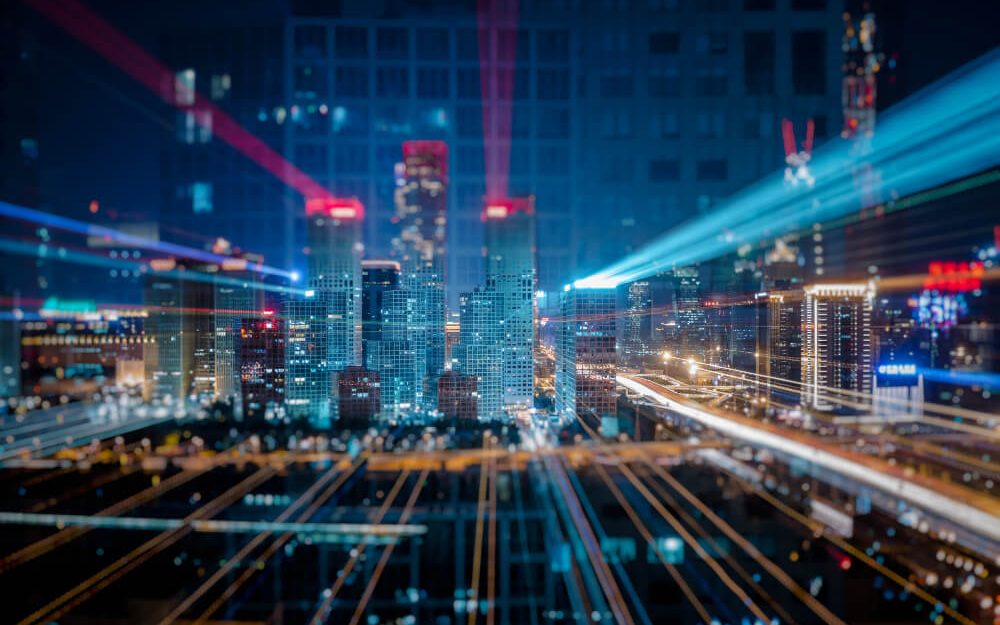 Imagem mostra cidade, com prédios altos e luminosidade. Mostrando algo mais tecnológico.
