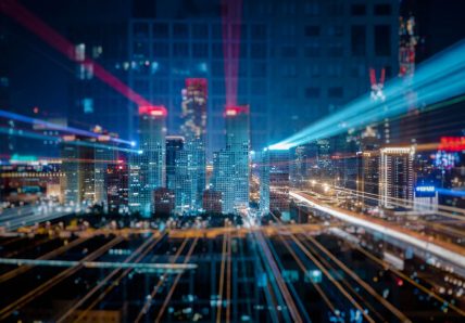 Imagem mostra cidade, com prédios altos e luminosidade. Mostrando algo mais tecnológico.