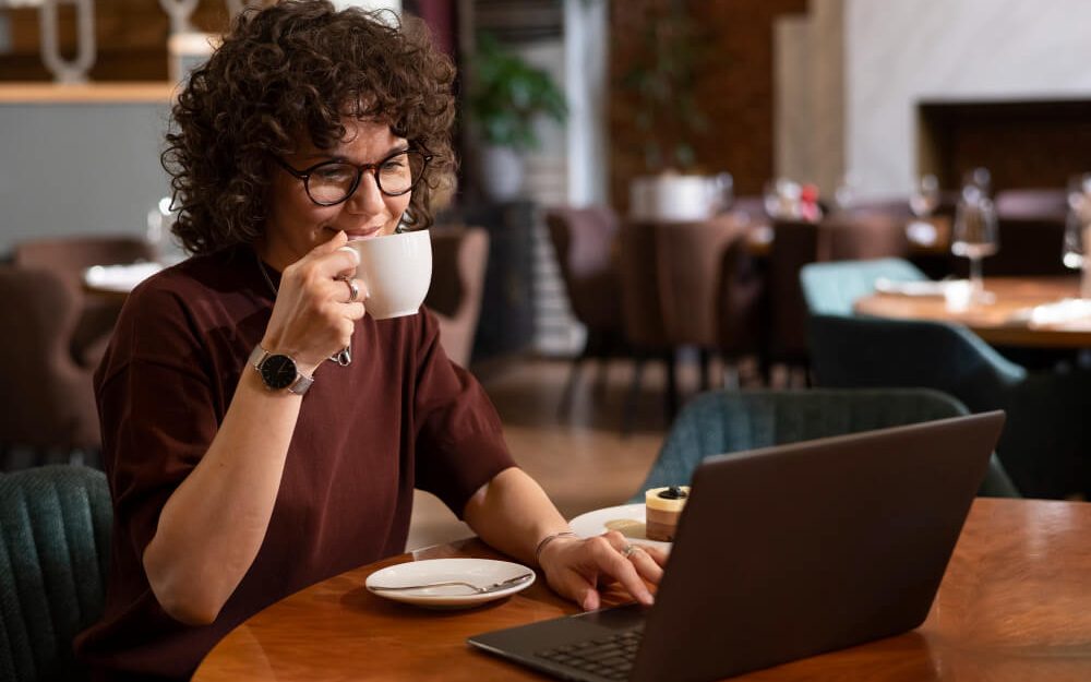 Imagem mostra mulher tomando um café enquanto trabalha em um escritório compartilhado